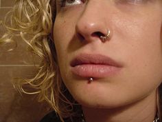 a woman with piercings on her nose in front of a tiled wall and floor