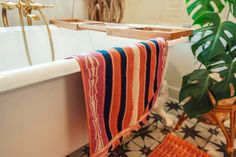 a towel hanging on the edge of a bathtub next to a potted plant