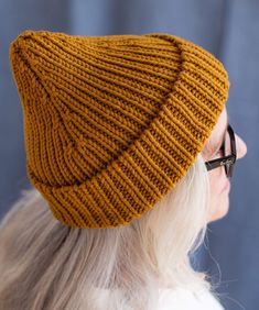 a woman wearing a mustard colored knitted beanie hat, looking off to the side