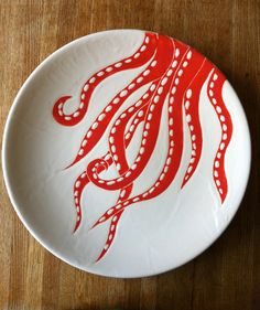 an octopus painted on a white plate with red trims sits on a wooden table