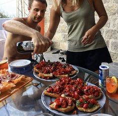 a man and woman are preparing food on a table outside with drinks in front of them