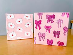 two pink canvases with bows and hearts on them sitting on a wooden table next to each other