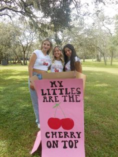 three girls standing behind a sign that says my littles are the cherry on top