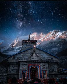 people are standing in front of a church under the night sky with mountains and stars