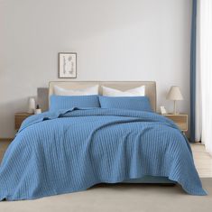 a bed with blue bedspread and pillows in a white room next to a window