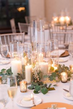 the table is set with candles, greenery and glass vases for centerpieces