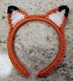 an orange and white crocheted cat ears headband on a marble counter top