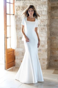 a woman standing in front of a brick wall wearing a white dress with short sleeves