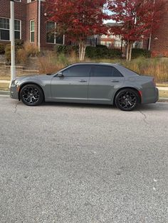 a gray car parked on the side of a road next to a tree with red leaves