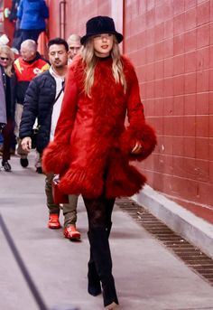 a woman in a red coat and hat walks down the street with other people behind her