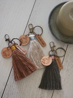 three tasseled key chains with personalized tags on them sitting next to a candle