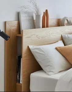 a bed with white sheets and pillows next to a book shelf filled with vases