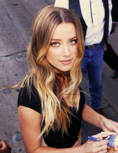 a woman with long blonde hair is looking at the camera while holding something in her hand