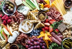 an assortment of cheeses, crackers, fruits and vegetables on a platter