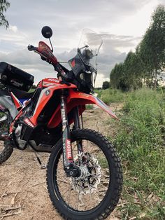 a red motorcycle parked on top of a dirt road