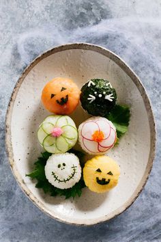 a white bowl filled with different types of sushi on top of a blue surface