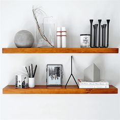 two wooden shelves with books, vases and other items on them against a white wall