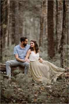 a man and woman sitting on a log in the woods