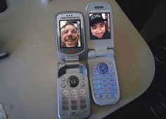 two cell phones sitting next to each other on top of a white table and one has an old man's face on the screen