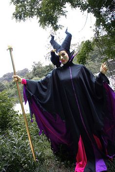 a woman dressed up as a witch holding a stick and wearing a black cape with purple trim