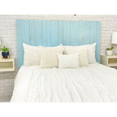 a bed with white sheets and pillows in front of a blue headboard on a brick wall