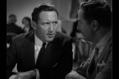 two men sitting at a table talking and one is wearing a suit with a tie