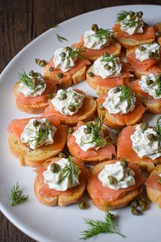 a white plate topped with crackers covered in cream cheese and smoked salmon slices, garnished with dill