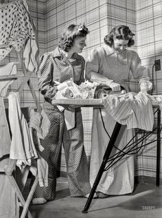 two women ironing clothes on an ironing board while another woman stands next to her