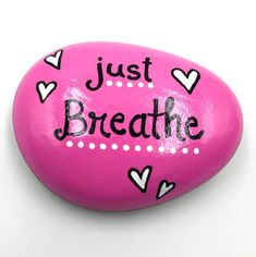 a pink rock with the words just breathe painted on it and hearts in black ink