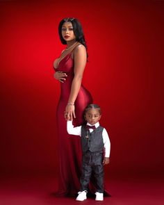 a woman in a red dress standing next to a little boy