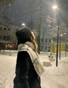 a woman is standing in the snow at night with her head turned to the side