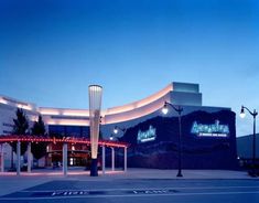 an empty parking lot in front of a large building with lights on the side and palm trees