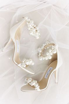 a pair of white high heel shoes with pearls on the toes and heels are shown in front of a veil