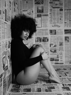 a black and white photo of a woman sitting on the floor in front of newspapers