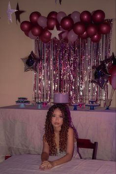 a young woman sitting at a table with balloons and streamers in the air above her head