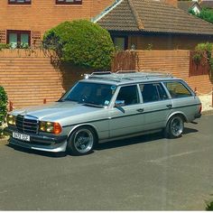 a silver station wagon parked in front of a brick building with trees and bushes behind it