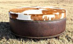 a brown and white cowhide ottoman sitting on top of dry grass