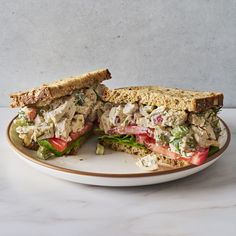 a chicken salad sandwich cut in half on a white plate with a marble counter top