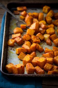 a pan filled with cooked sweet potatoes on top of a blue cloth next to a spoon