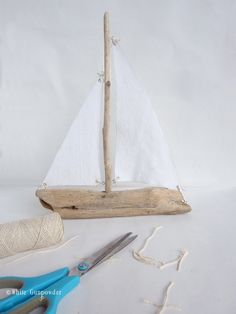 a wooden sailboat sitting on top of a white table next to scissors and twine