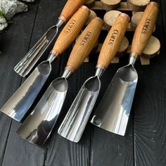 four stainless steel utensils with wooden handles and engraved names on them sitting next to logs