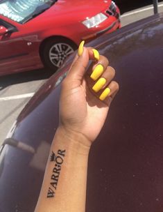 a woman's arm with yellow nail polish on it and a red car in the background