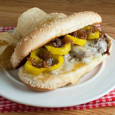 a sandwich with cheese, peppers and onions on a white plate next to some potato chips