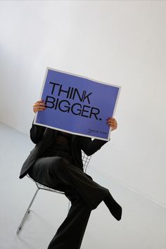 a person sitting in a chair holding a sign that says think bigger