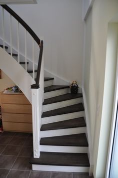 a white and black stair case next to a brown tiled floor in a room with beige walls