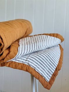 two folded blankets sitting on top of a white stool next to a wall and floor