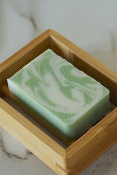 a green and white soap bar sitting in a wooden tray on a marble counter top