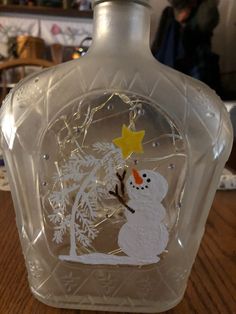 a glass bottle with a snowman and tree on the top, sitting on a table