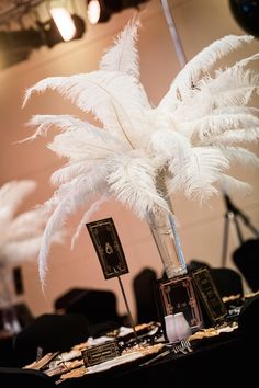 there is a tall white feather centerpiece in the middle of a table with place cards on it