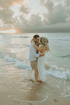 a man and woman standing on top of a beach next to the ocean holding each other